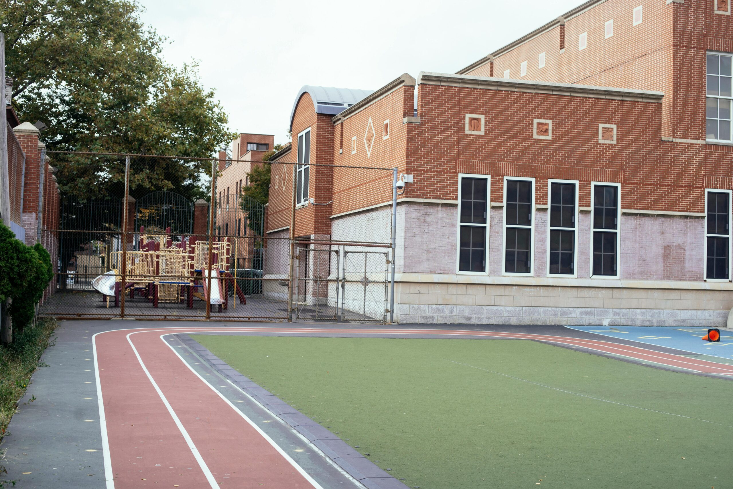 Empty urban schoolyard featuring a red brick building, playground, and athletic track, captured during daytime.