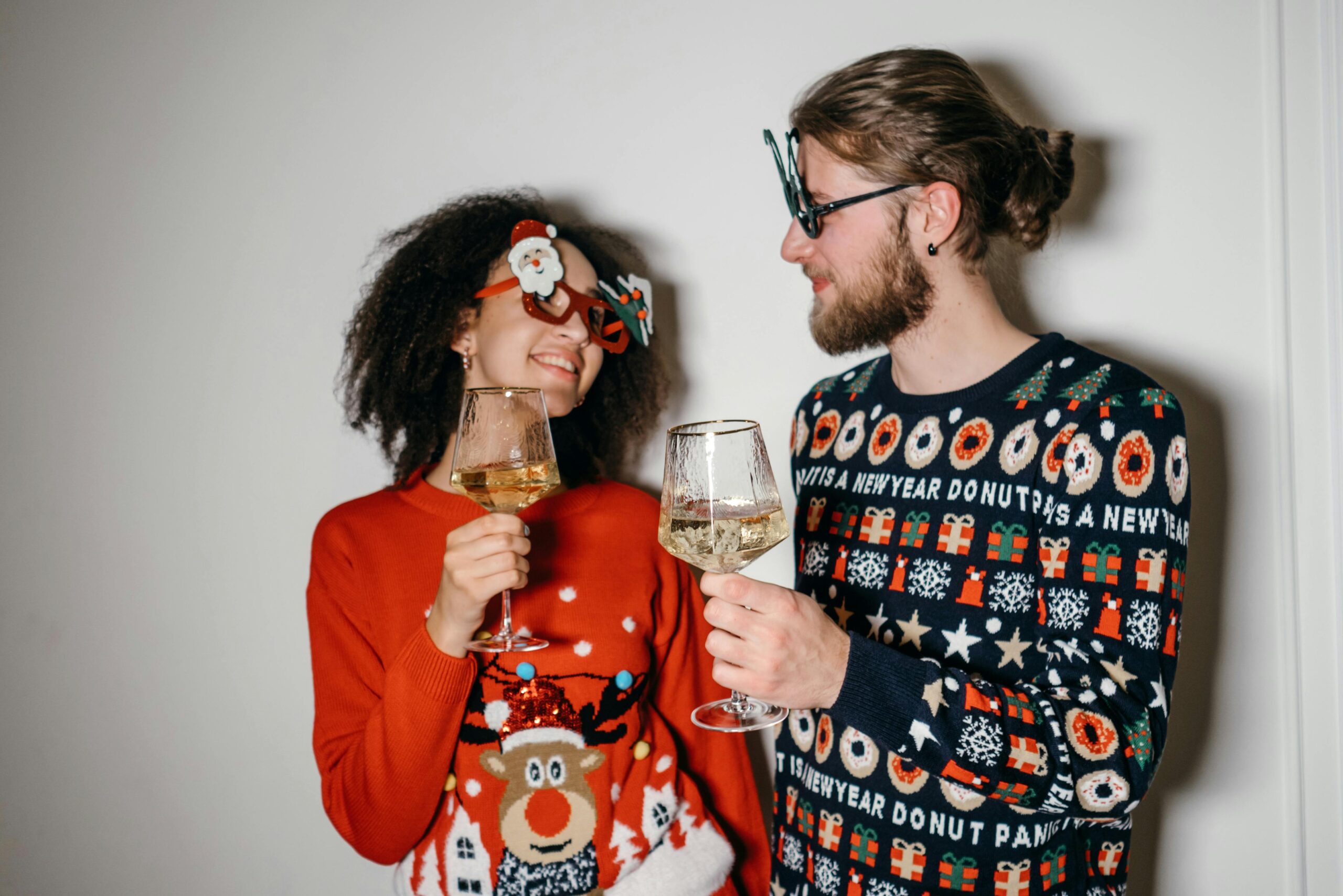 A joyful couple in holiday sweaters toasting with wine glasses during a Christmas celebration.