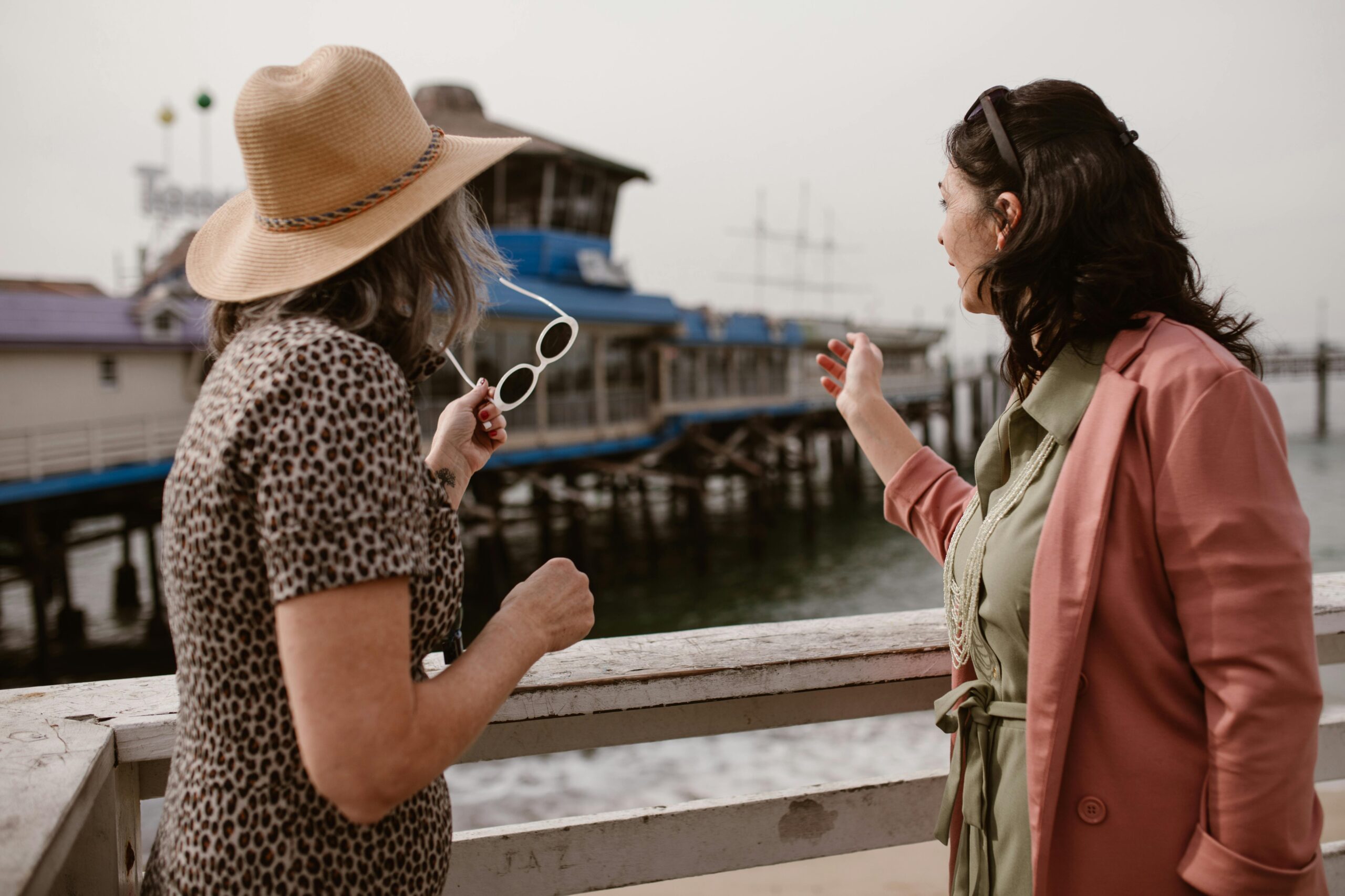 Two women at a pier, enjoying a day by the sea, sharing a moment.