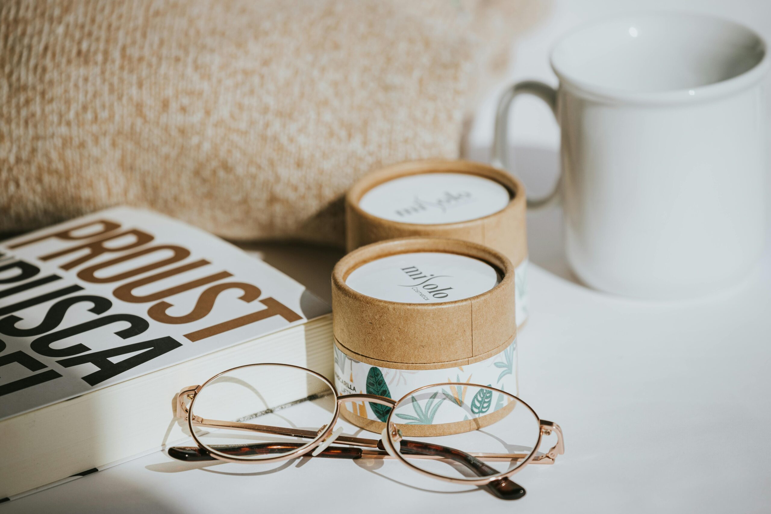 A cozy still life with glasses, a book, coffee cup, and candles in natural light.