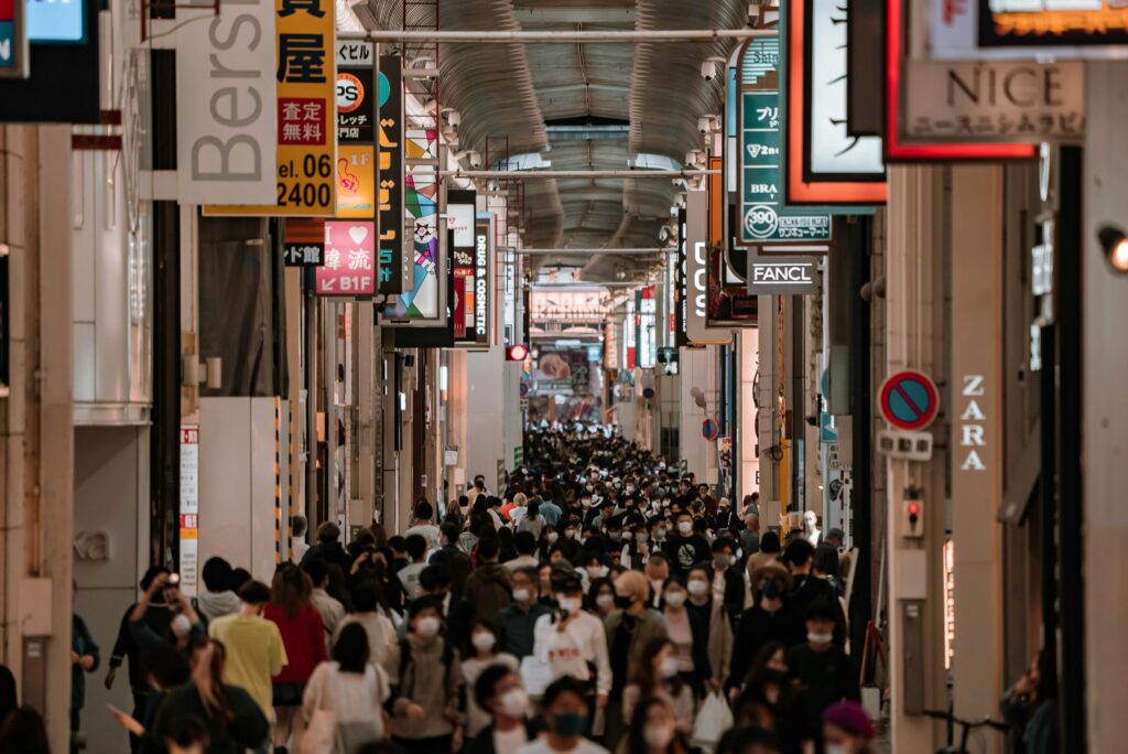 Crowded shopping street in Osaka, Japan filled with people and vibrant store signs.