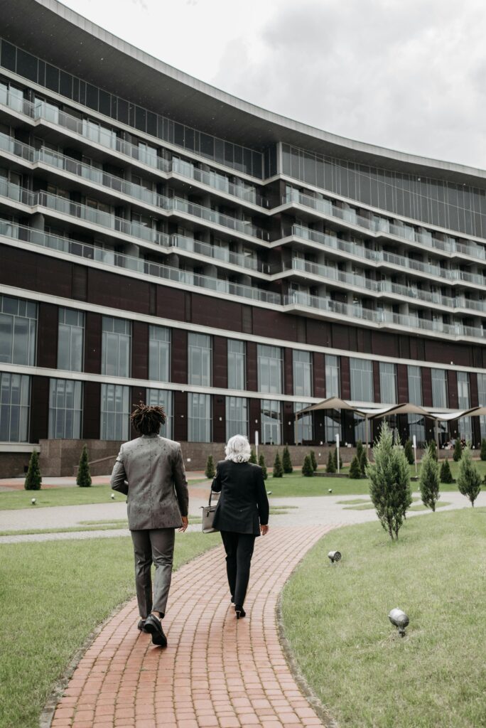 Two business individuals walking towards a modern glass building, showcasing professional attire and outdoor architecture.