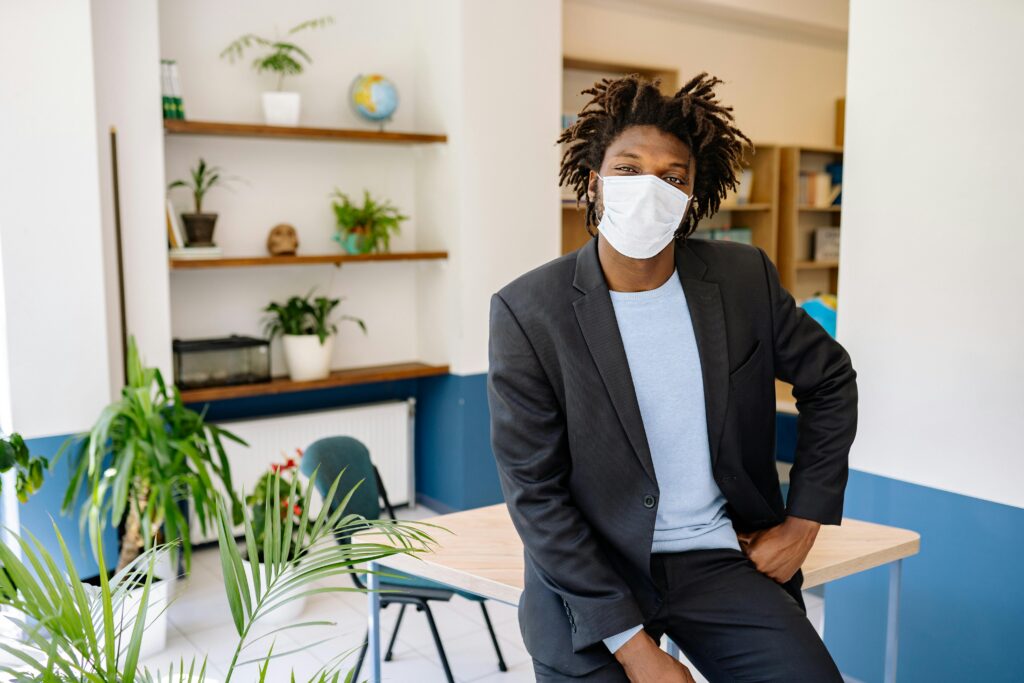 African American man in suit with face mask seated in modern office environment.