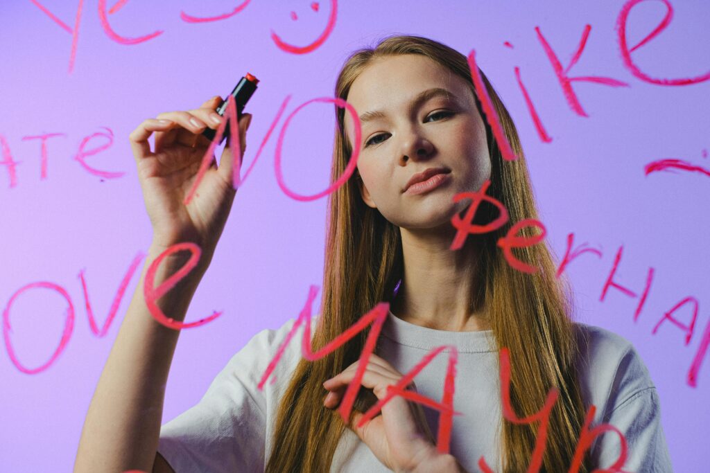 Teen girl in studio writes on glass with pink marker, expressing emotions.