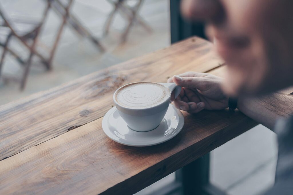A man holds a cup of coffee with latte art in a cozy cafe, perfect for relaxation.