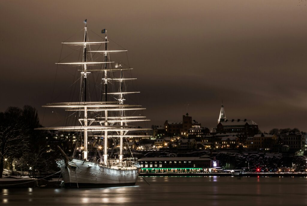 A majestic illuminated sailboat moored in Stockholm's harbor at night, showcasing beautiful city lights.