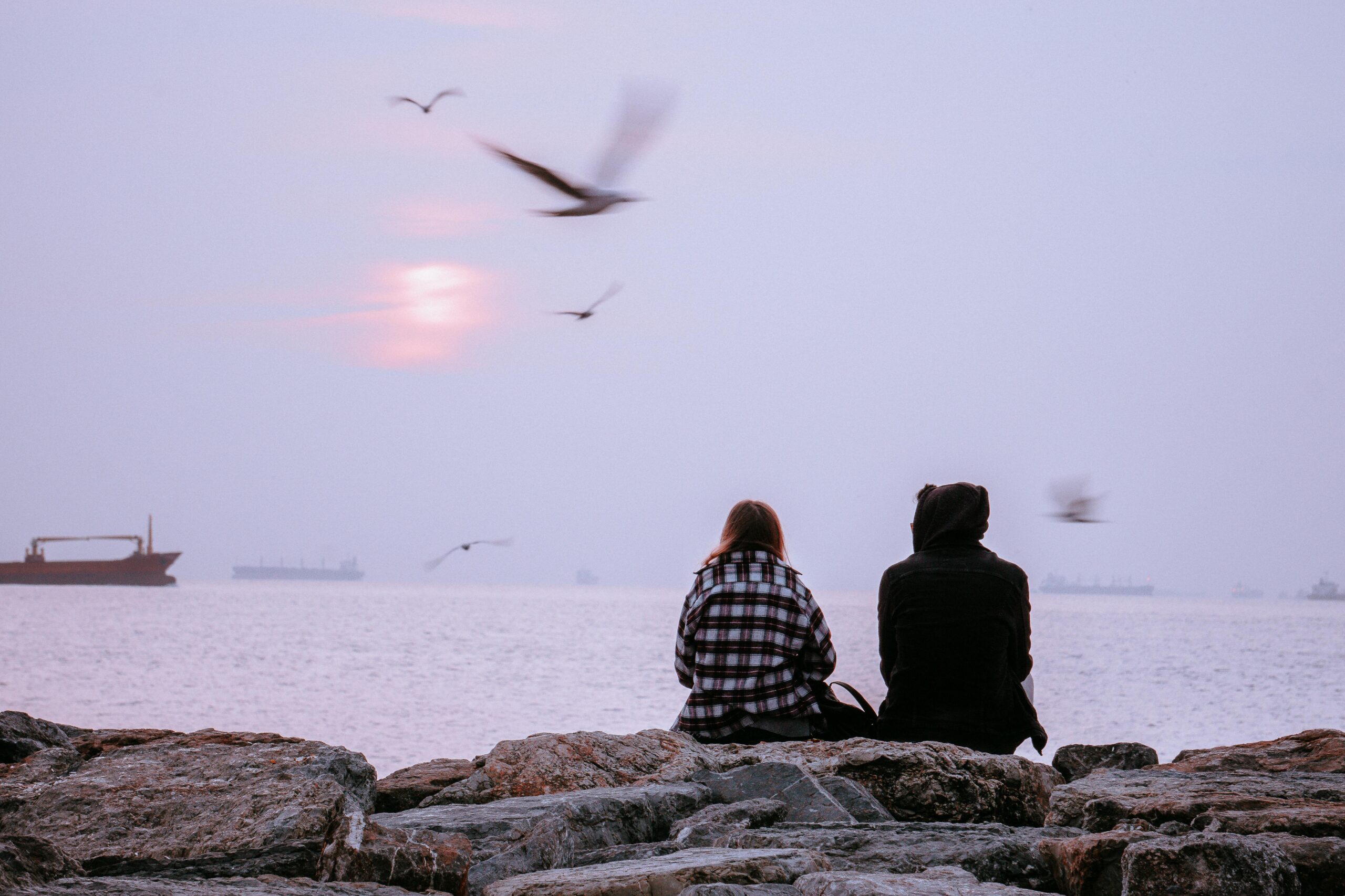A couple sits on rocks watching the sunset over the Istanbul sea, surrounded by birds.