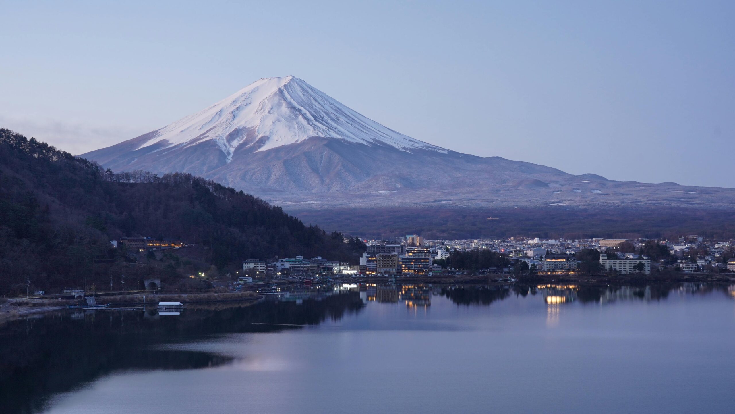 A serene sunset view of Mount Fuji reflected in a calm lake with a nearby town.