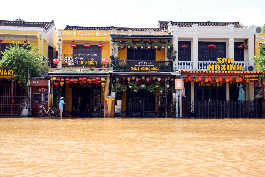 Flooded street in Hoi An, showcasing colorful facades and lanterns with reflections in the water.
