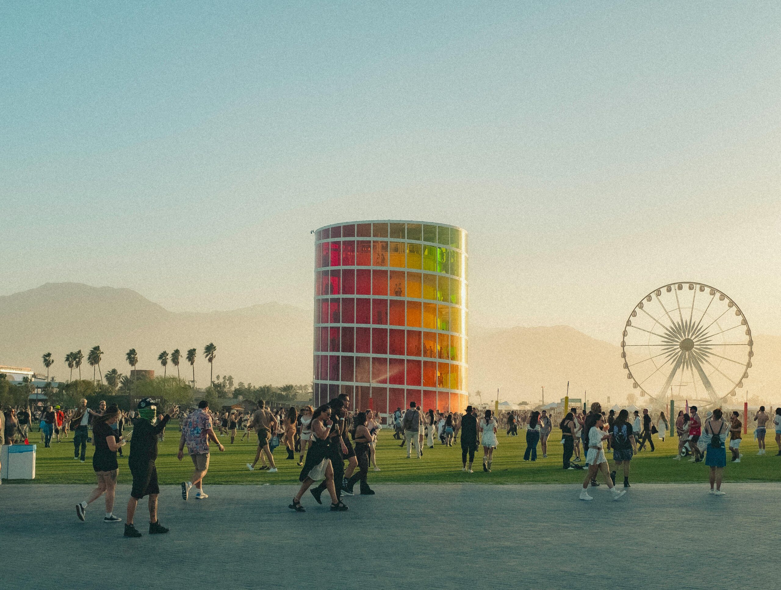 People enjoying a lively music festival with a colorful tower and Ferris wheel backdrop.