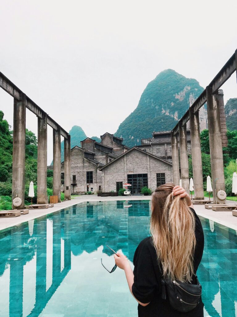 Woman at luxurious resort pool with mountain backdrop and unique architecture.
