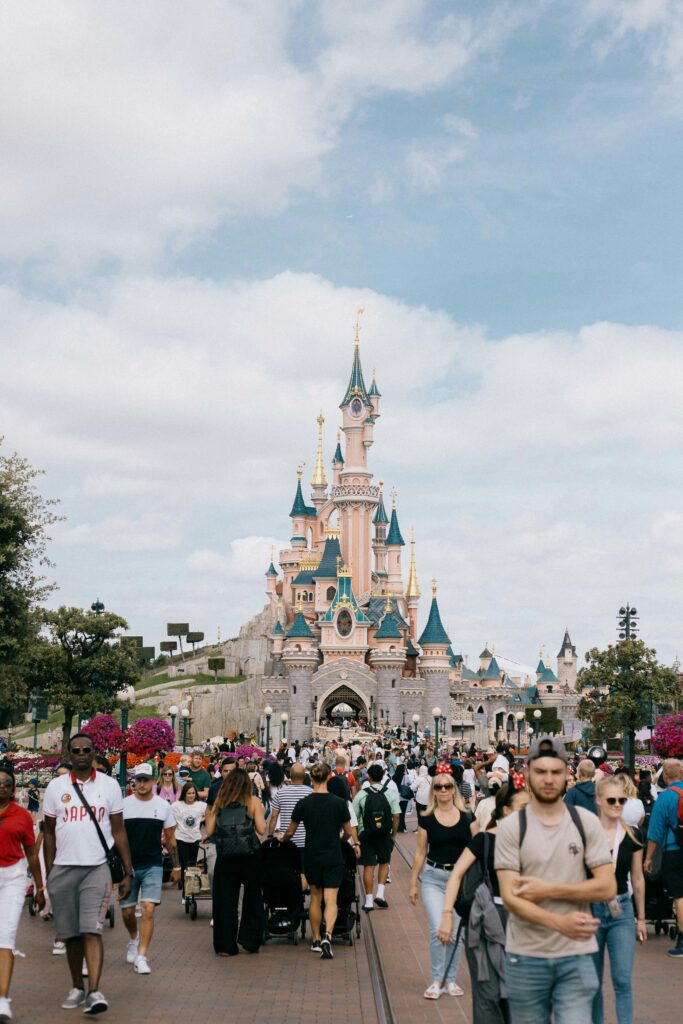 A lively crowd enjoying a day at Disneyland Paris with Sleeping Beauty Castle in view under a bright sky.