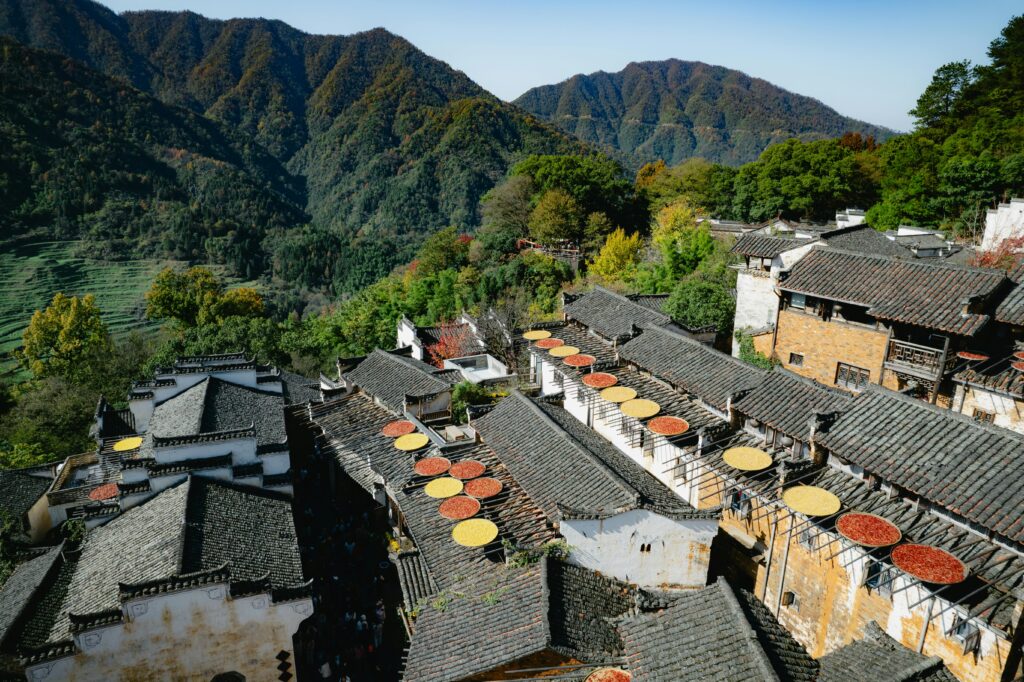 Scenic view of traditional Chinese village with rooftops and drying racks set against mountainous landscape.