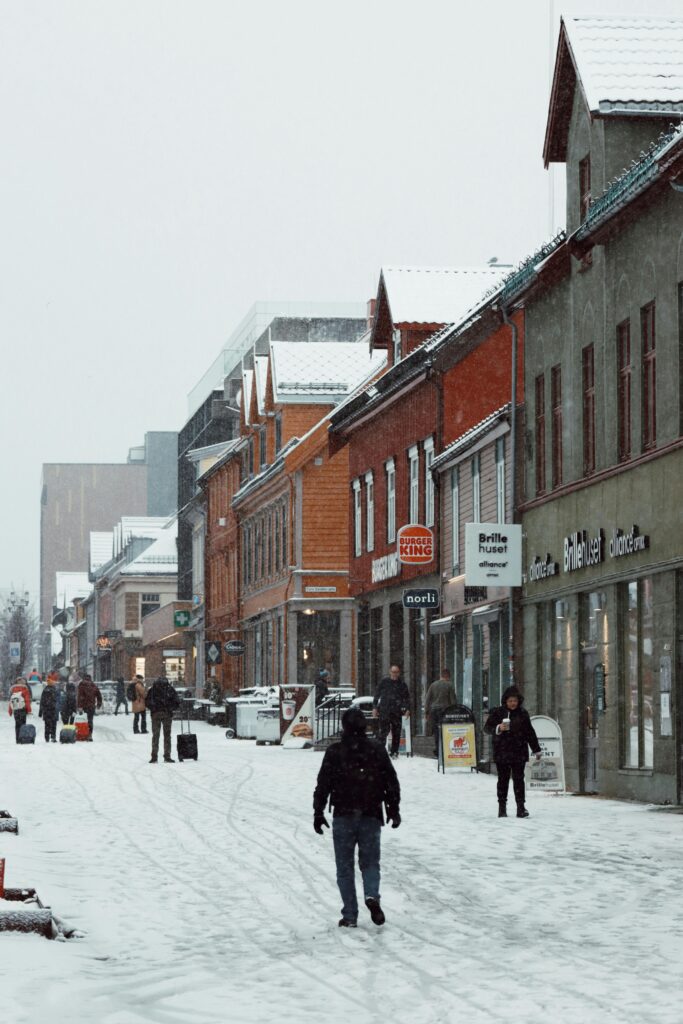 Charming winter street in Tromsø, Norway, with people and snow-covered buildings.