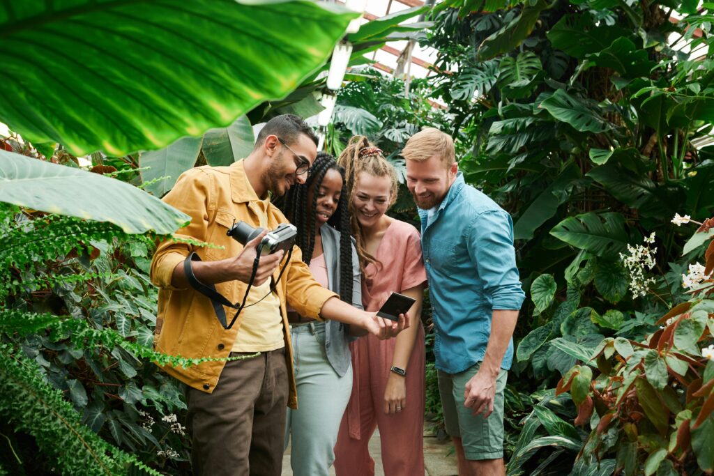 Friends gather in a lush greenhouse to share instant camera photos, capturing happy memories.
