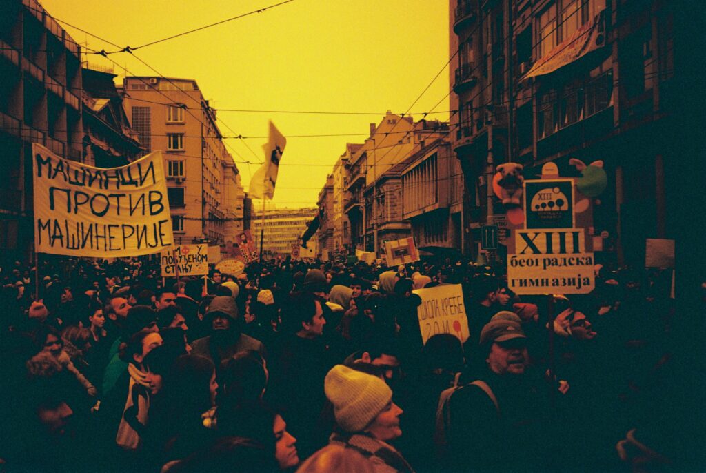 Large crowd demonstrating with banners in urban city street, vibrant atmosphere.