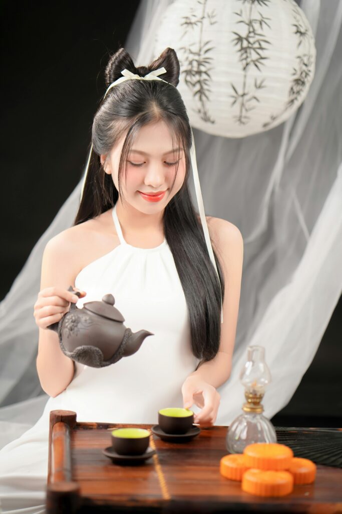 Asian woman in a tranquil indoor setting pouring tea from a traditional teapot into cups.