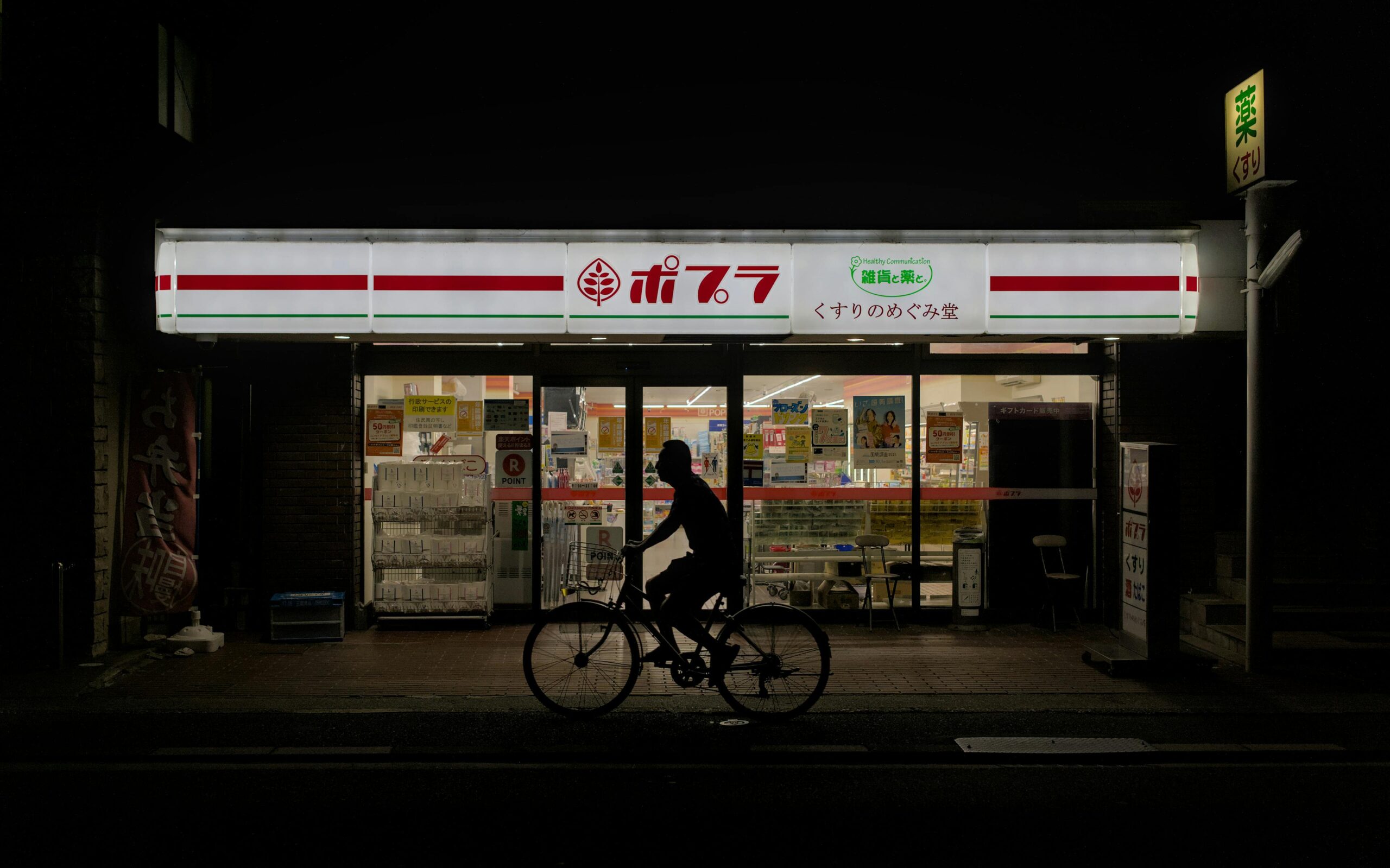 A cyclist passing by a convenience store at night in Kyoto, Japan.