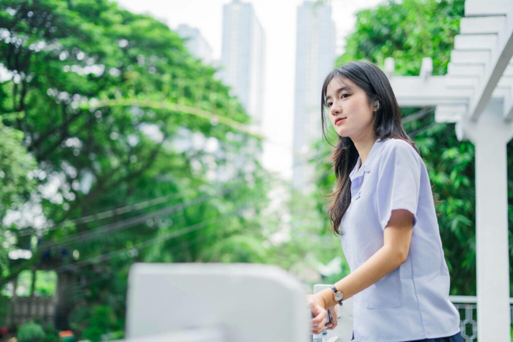 Portrait of a young woman outdoors, surrounded by greenery and city buildings.