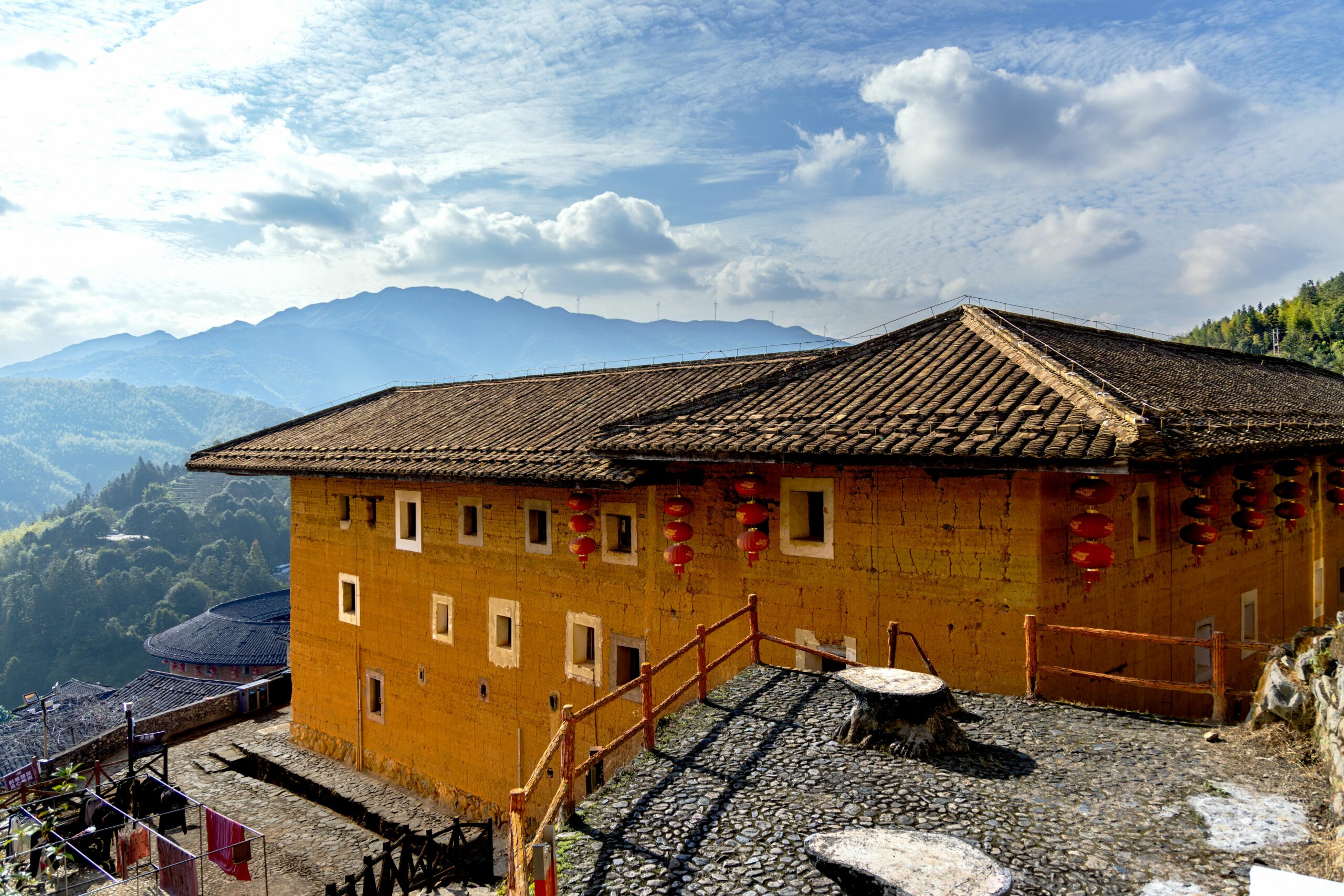 Scenic view of a traditional Fujian Tulou with mountains in the background under clear skies.