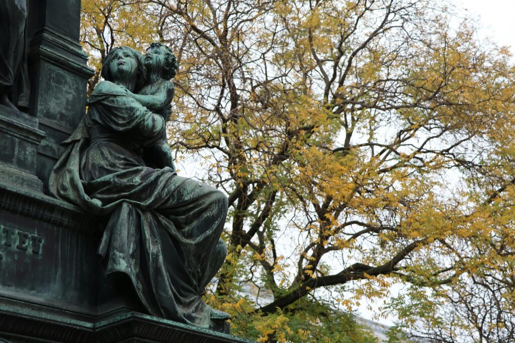 A bronze statue set against vibrant autumn leaves in Vienna, Austria, showcasing artistic craftsmanship.
