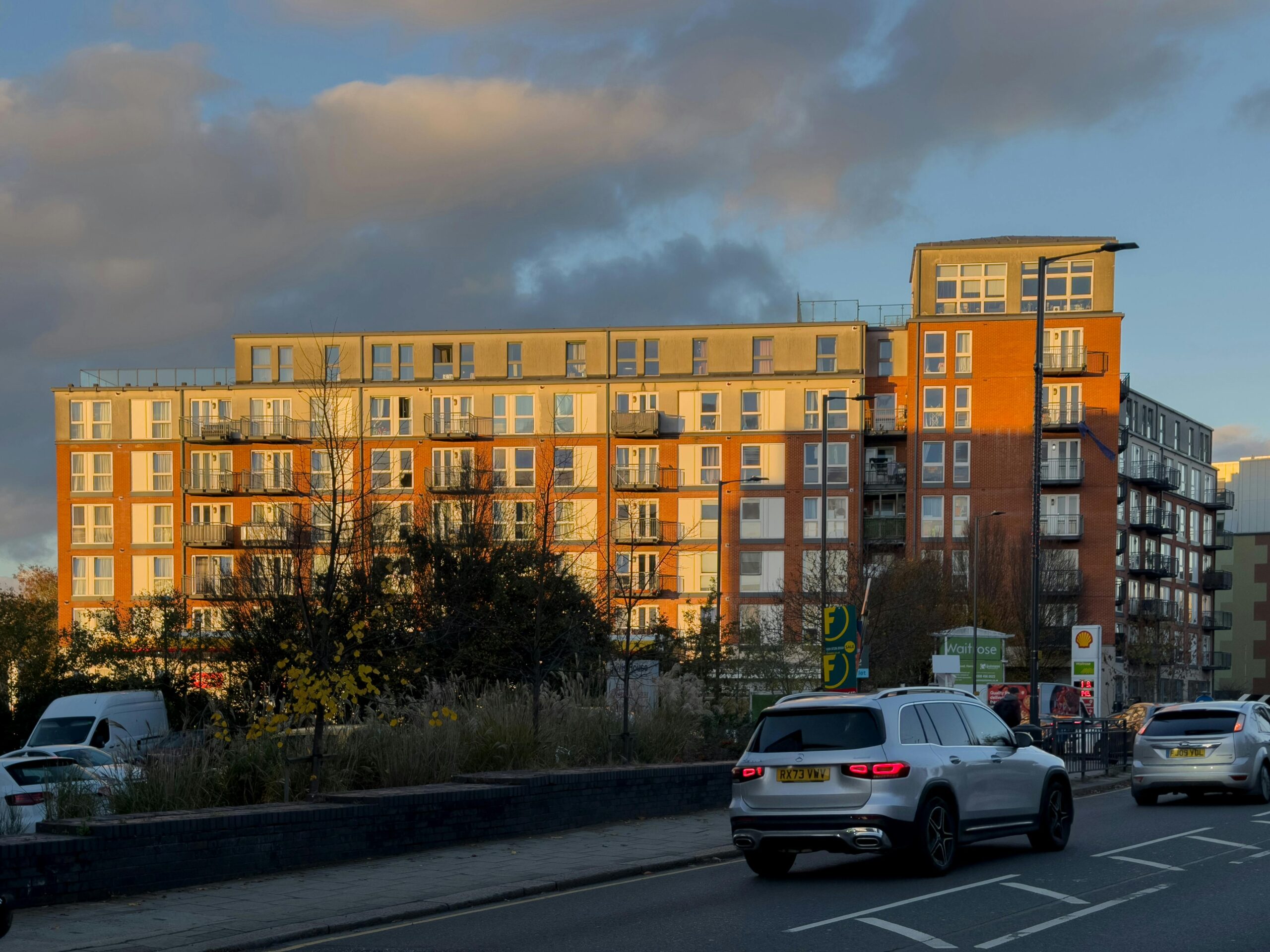 Sunlit modern apartment complex with street traffic at dusk.