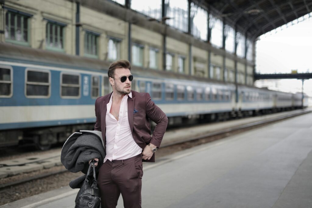 A fashionable man in sunglasses and suit waiting at an urban train station. Perfect for business-related themes.