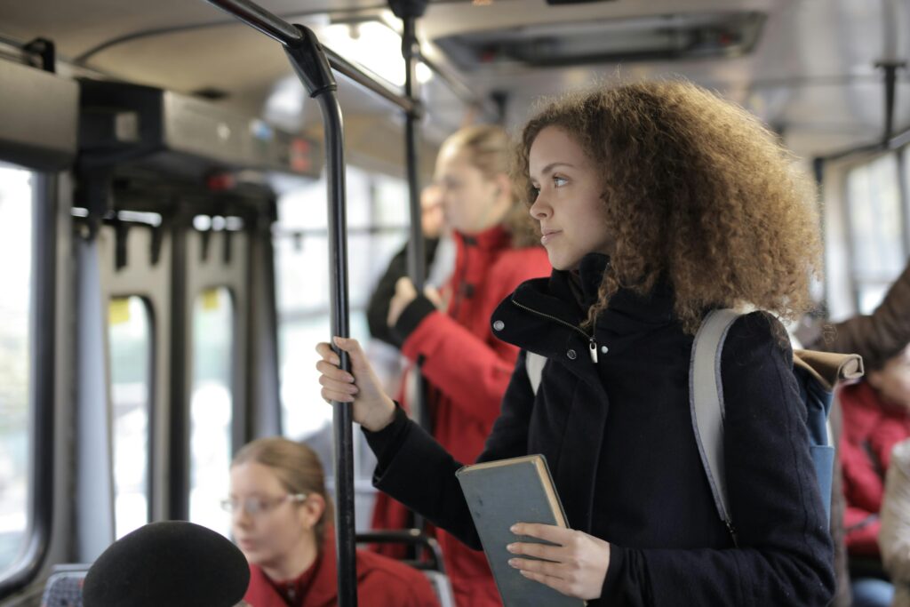 A young woman with curly hair reads a book while riding a public bus.