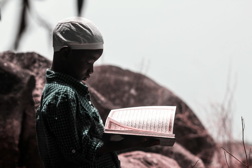 A young boy reading the Quran outdoors in Abuja, Nigeria, symbolizing faith and learning.