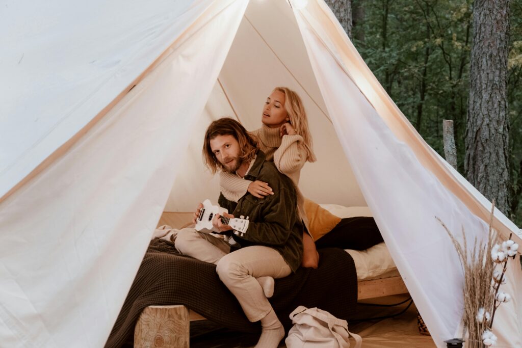 Couple relaxing in a tent with a ukulele, enjoying cozy woodland glamping.