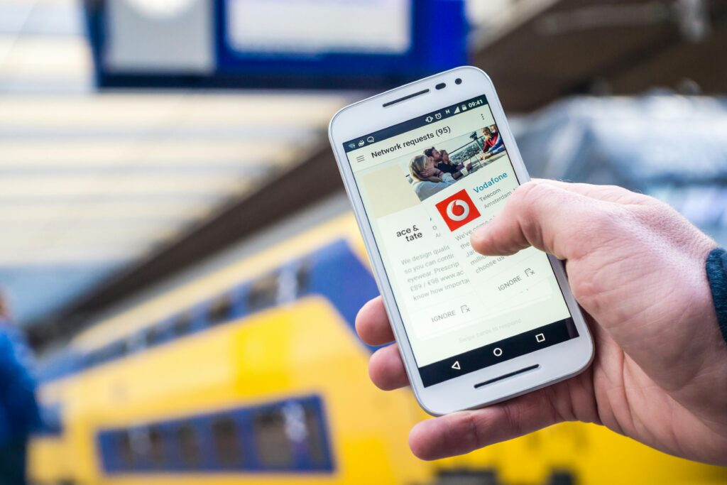 Close-up of a person using a smartphone with a train in the background, outdoors.