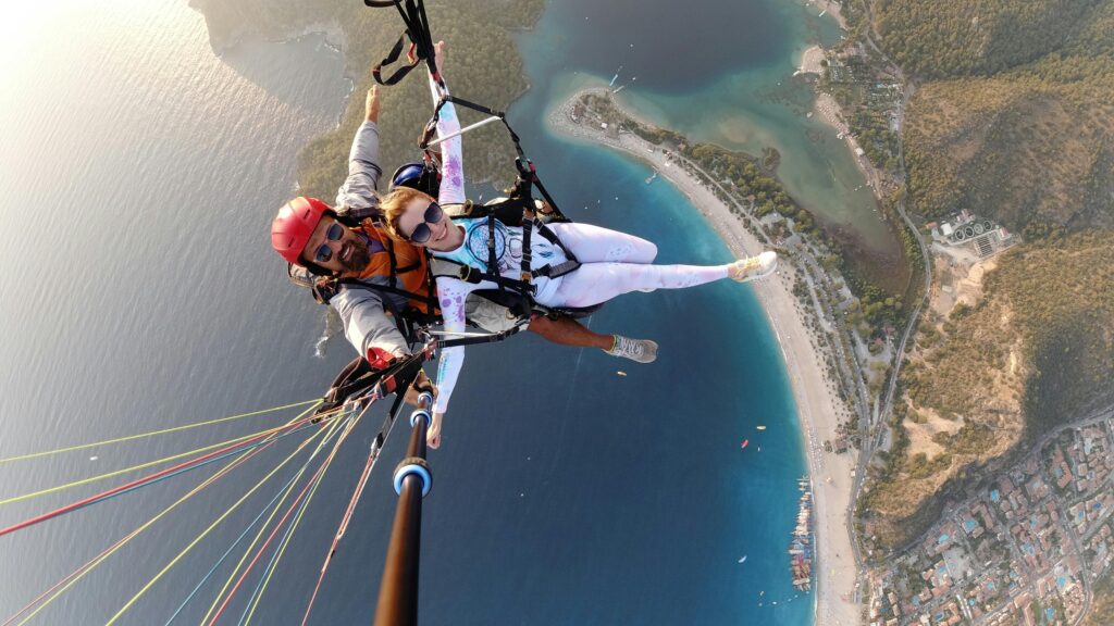 Dynamic aerial view of a joyful couple paragliding above the coastline, capturing an adventurous selfie.