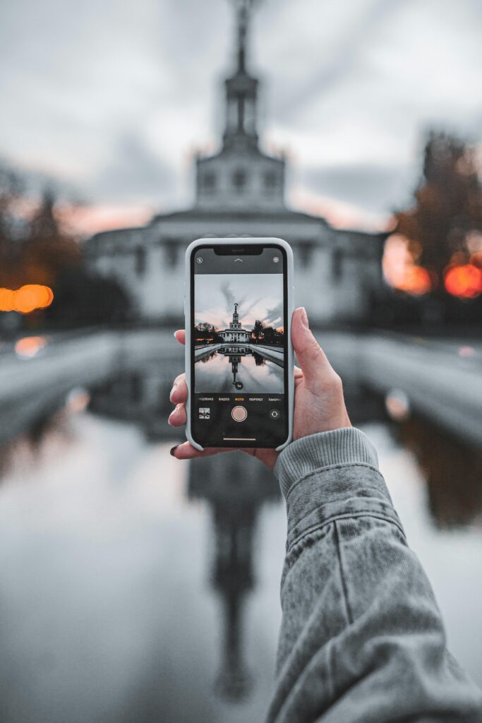 Smartphone capturing a building reflection in a peaceful outdoor setting.