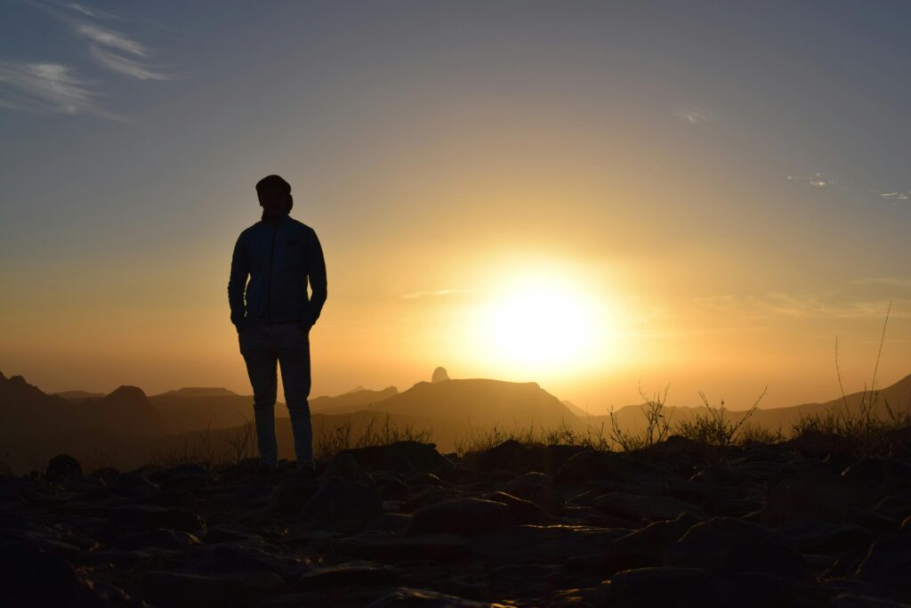 A lone silhouette of a man stands against a breathtaking sunset in the Amguel desert, Tamanrasset Province, Algeria.