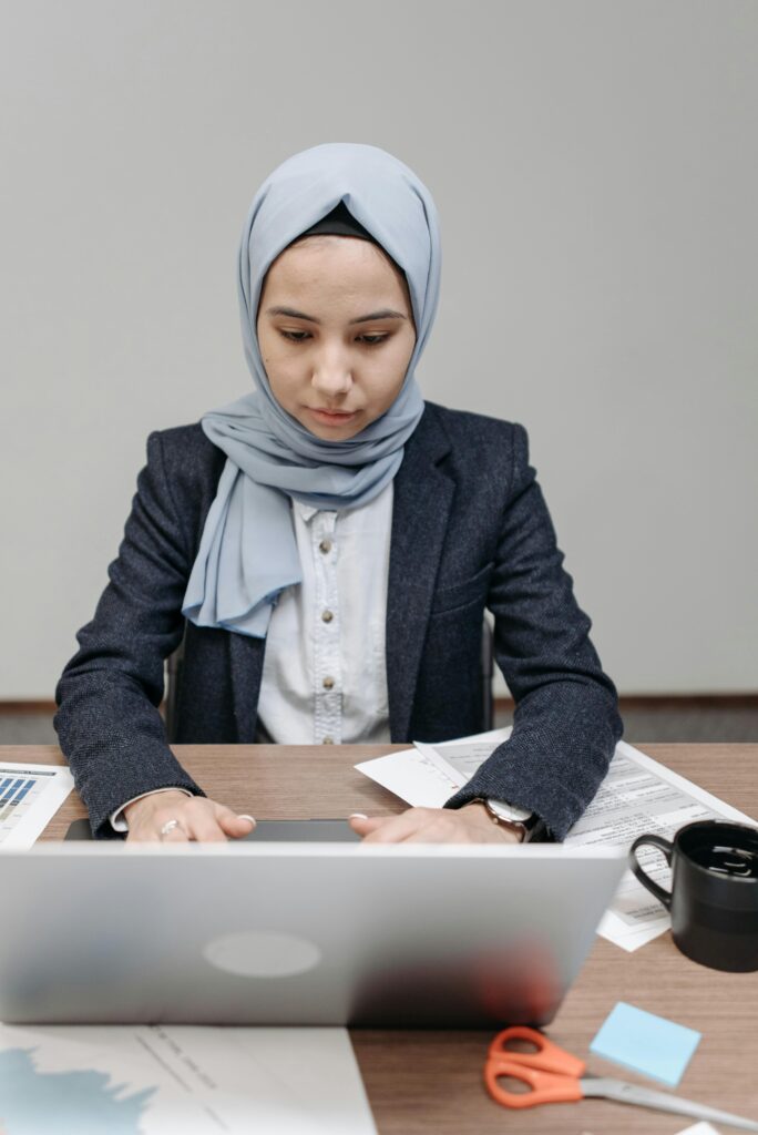 Professional Muslim woman in hijab focused on laptop work at her desk.
