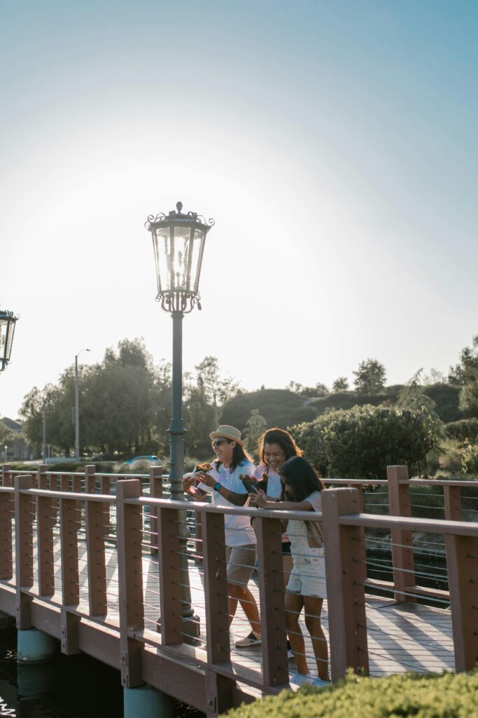 Family enjoying a sunny day walk on a footbridge in a picturesque park setting.