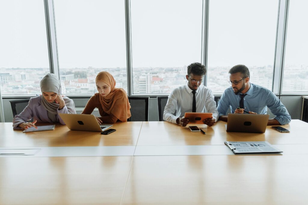 A diverse group of colleagues working together using laptops and tablets in a modern office setting.