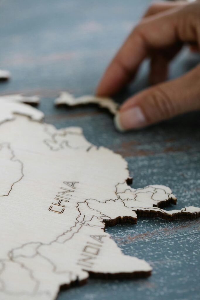 Hand adjusting wooden map piece representing countries like China and India, selective focus.