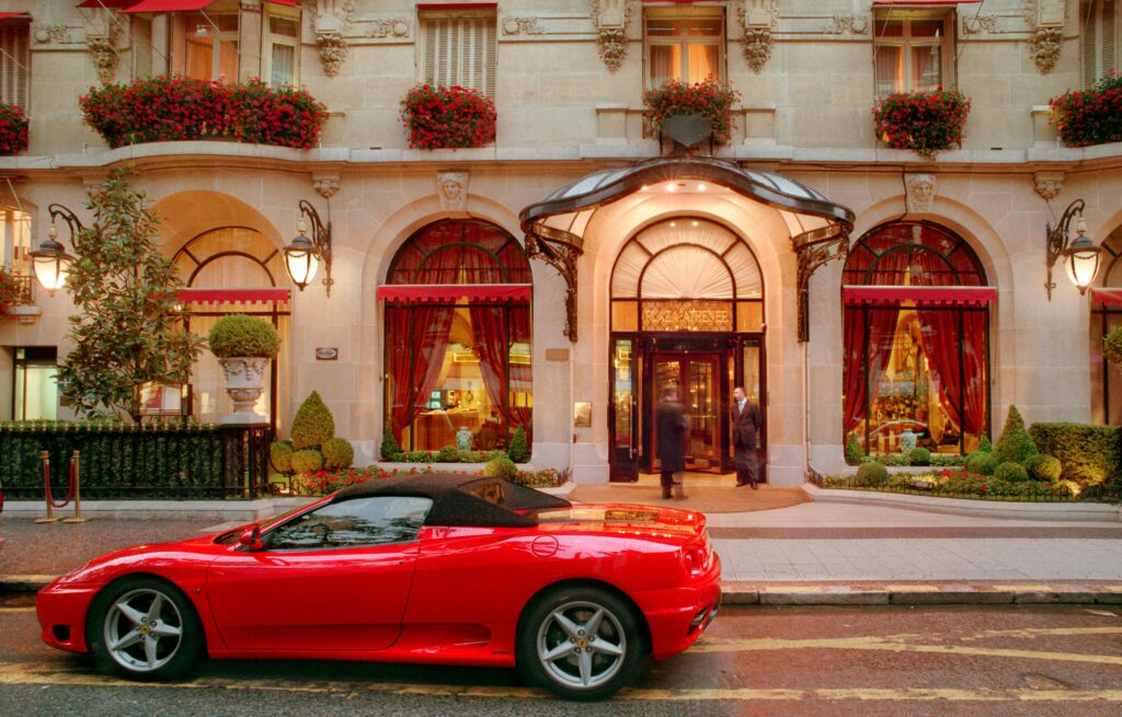 Red sports car parked outside a lavish hotel entrance at night, showcasing opulence.
