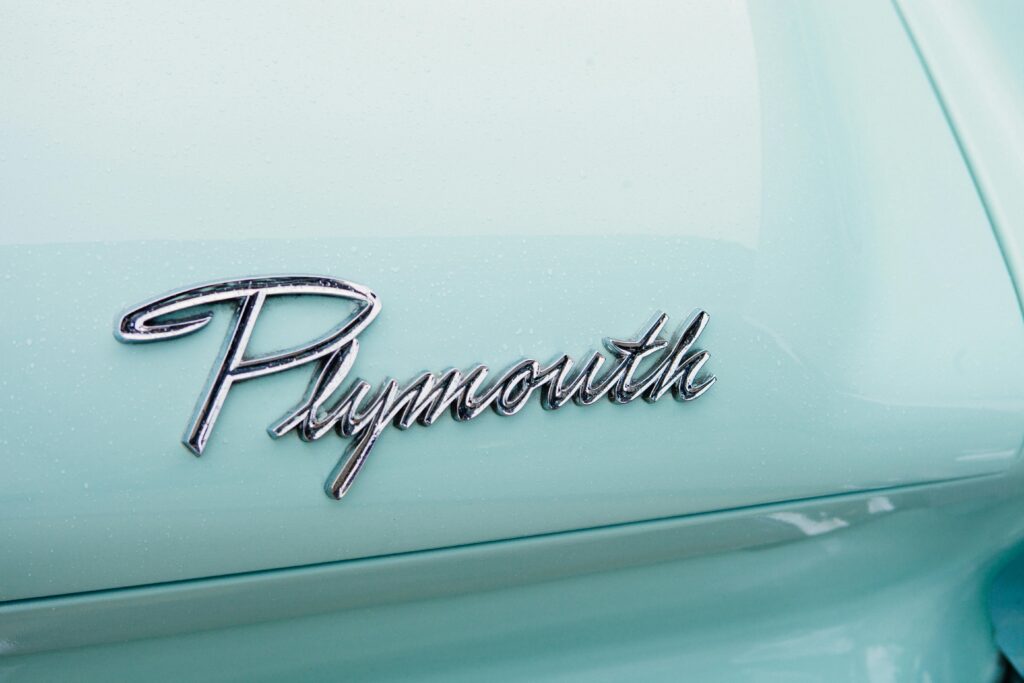 Chrome Plymouth emblem on vintage car with light blue paint and sleek design.