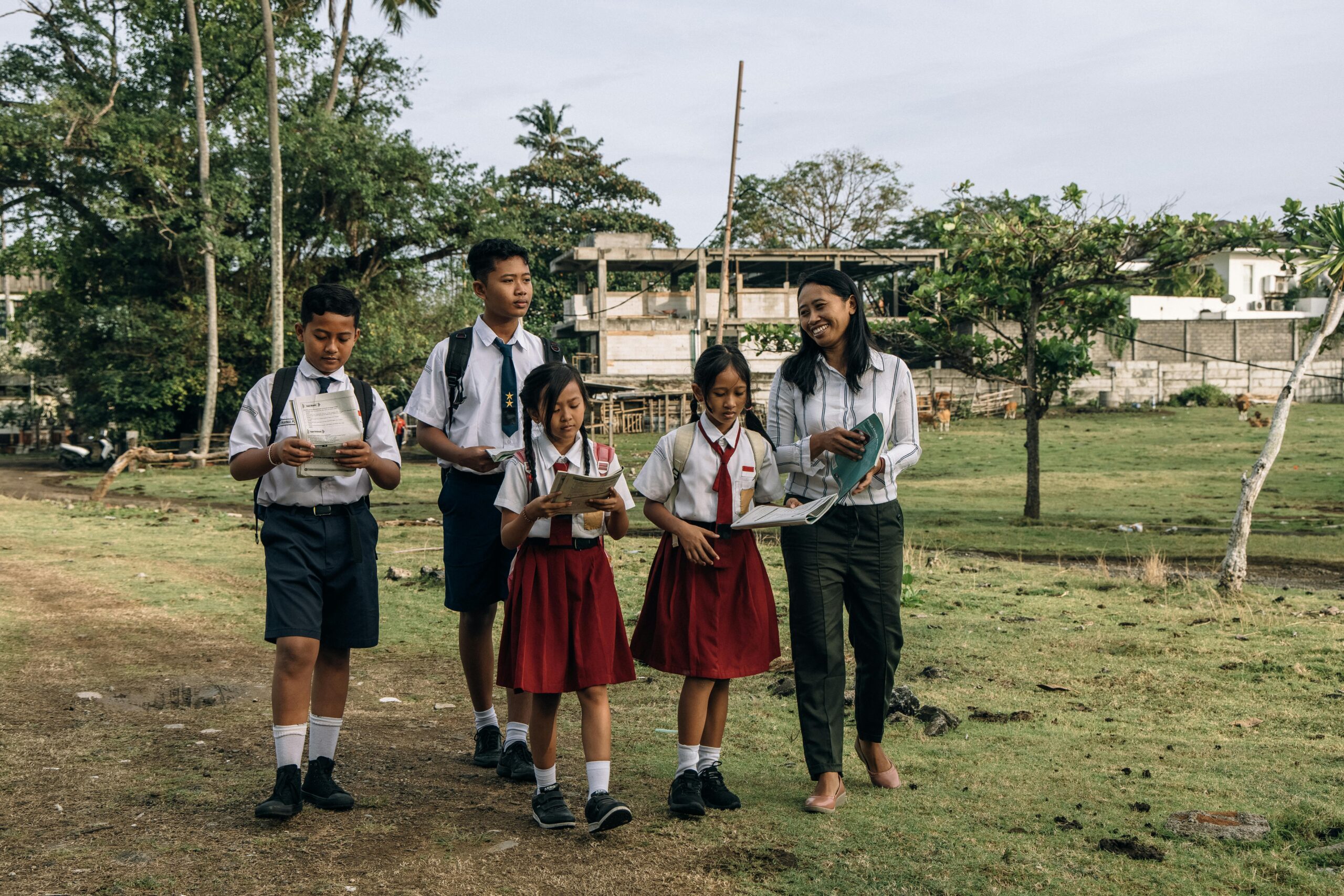 Group of students in uniforms, walking with their teacher in a rural setting.