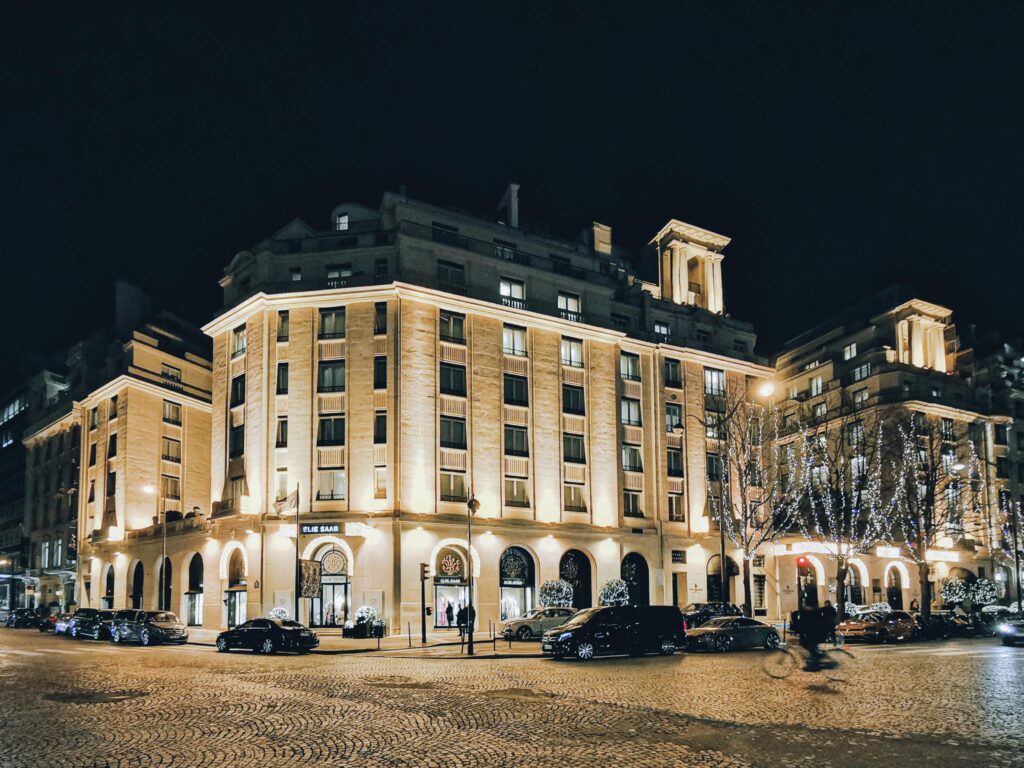 A stunning city street at night featuring illuminated building facades and parked cars under streetlights.