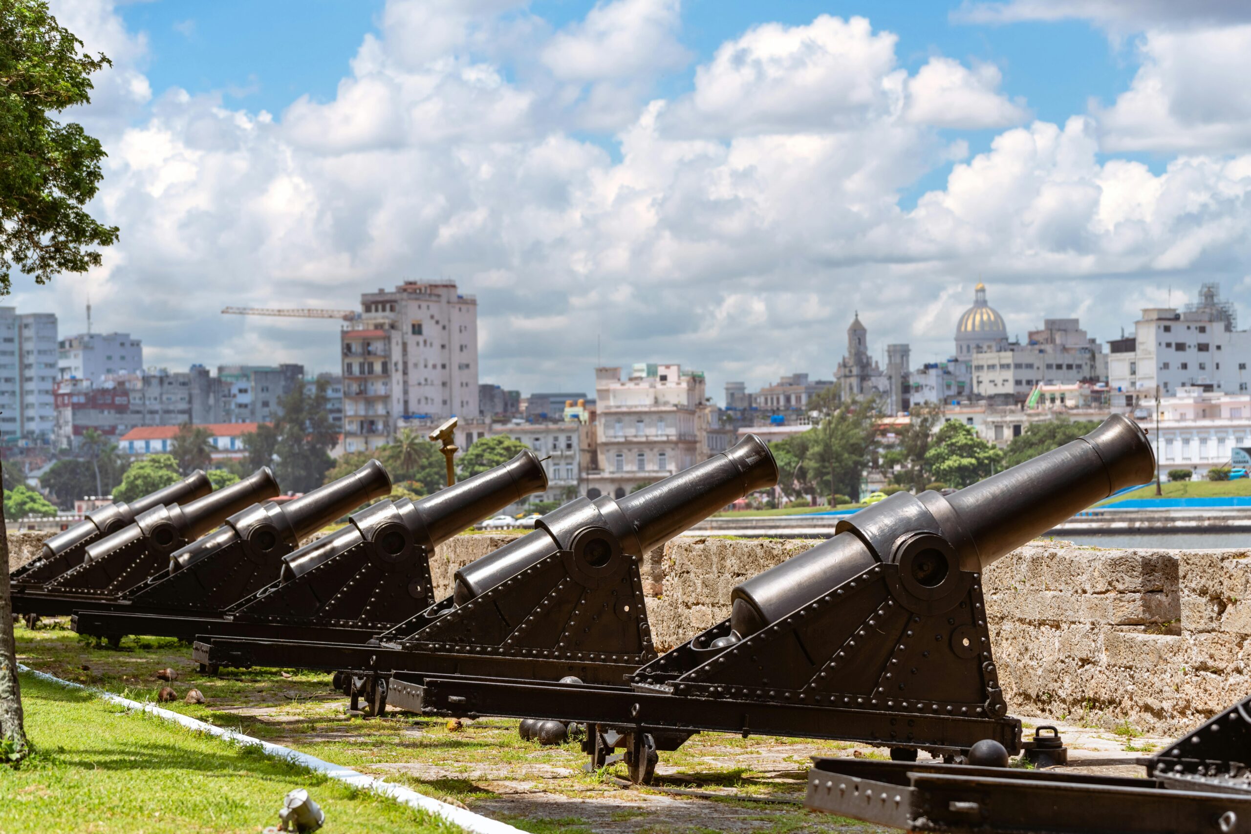 Row of historic cannons facing Havana's vibrant cityscape on a sunny day.