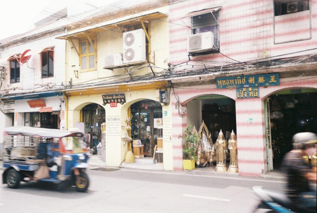 Tuk-tuk speeds past colorful shops in vibrant downtown Bangkok, Thailand.