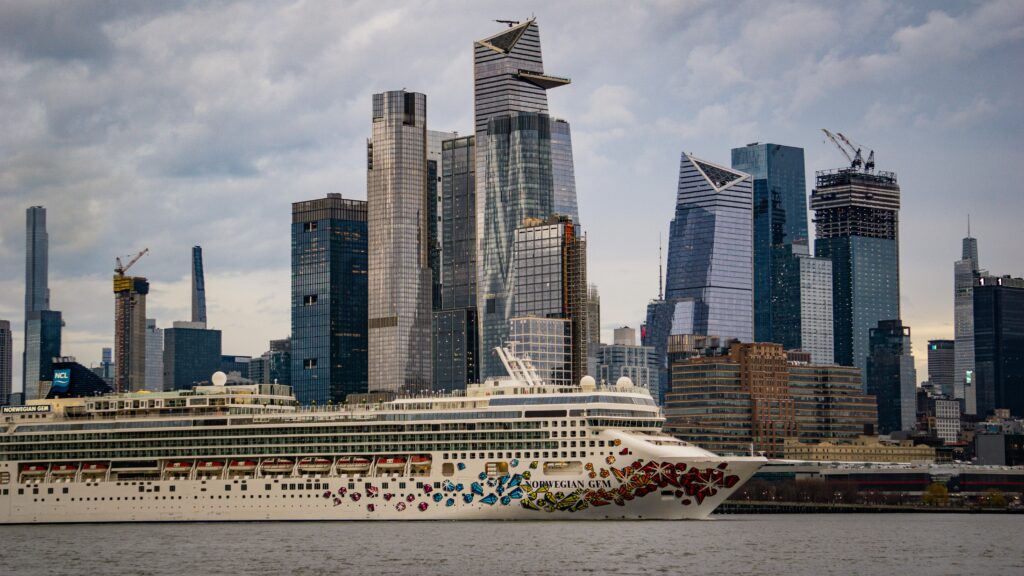 Norwegian Gem cruising past the iconic skyline of New York City with modern skyscrapers.