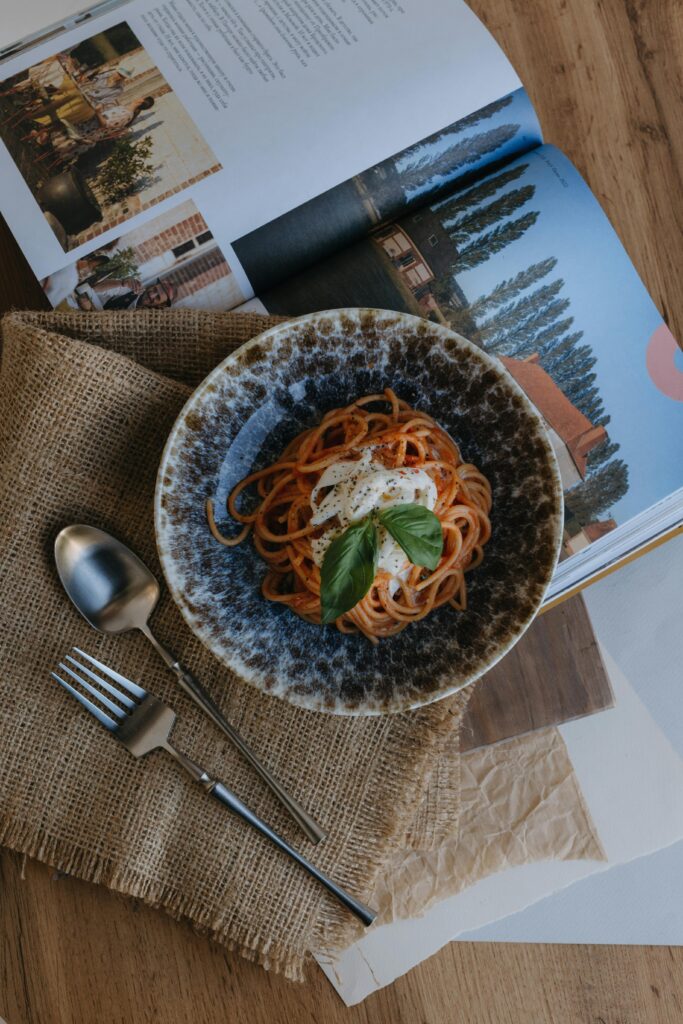 Delicious spaghetti served with basil and cheese on rustic table with an open cookbook nearby.