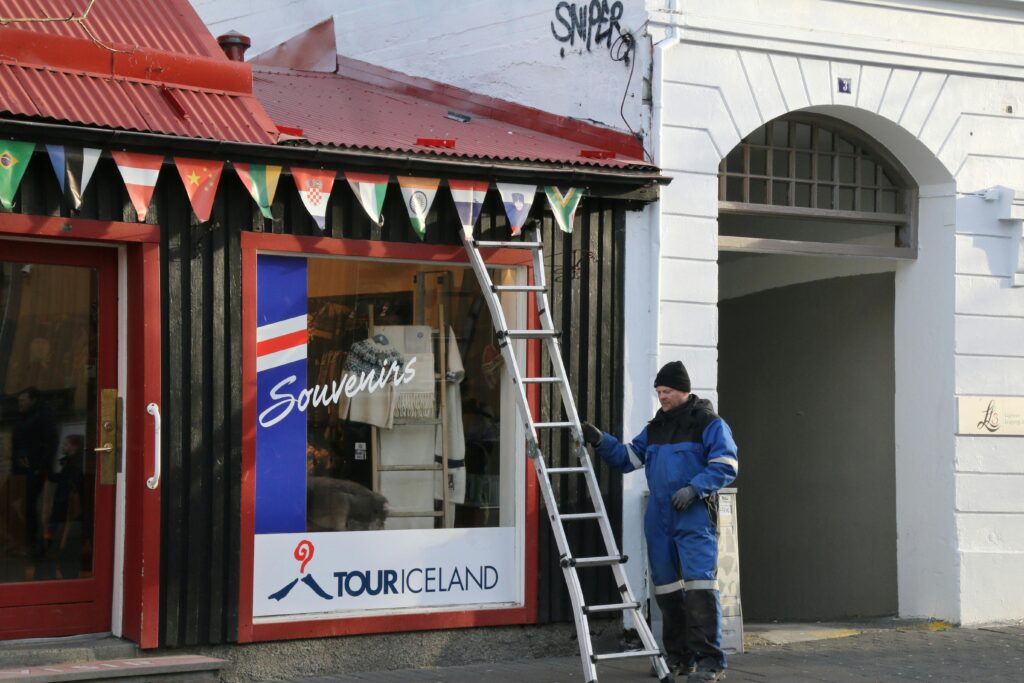 A worker standing outside a Reykjavik souvenir shop with international flags and a ladder.