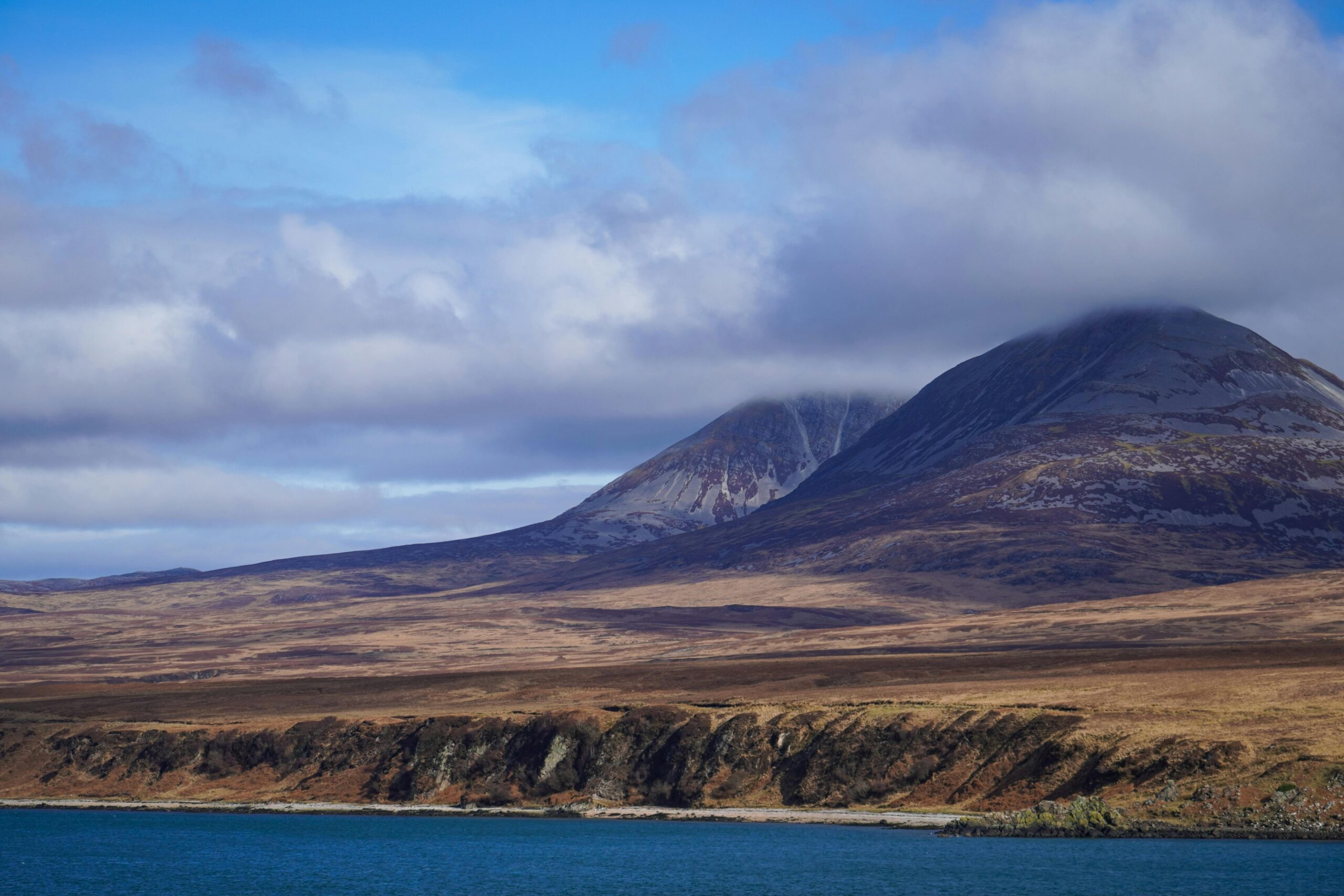 Breathtaking view of the Paps of Jura in the Inner Hebrides, Scotland with cloudy skies and coastal landscape.