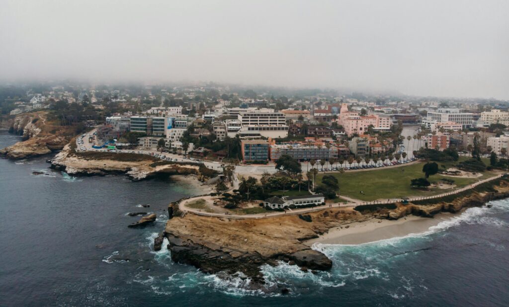 Aerial shot of La Jolla Cove in San Diego, California, showcasing coastal cliffs, cityscape, and foggy atmosphere.