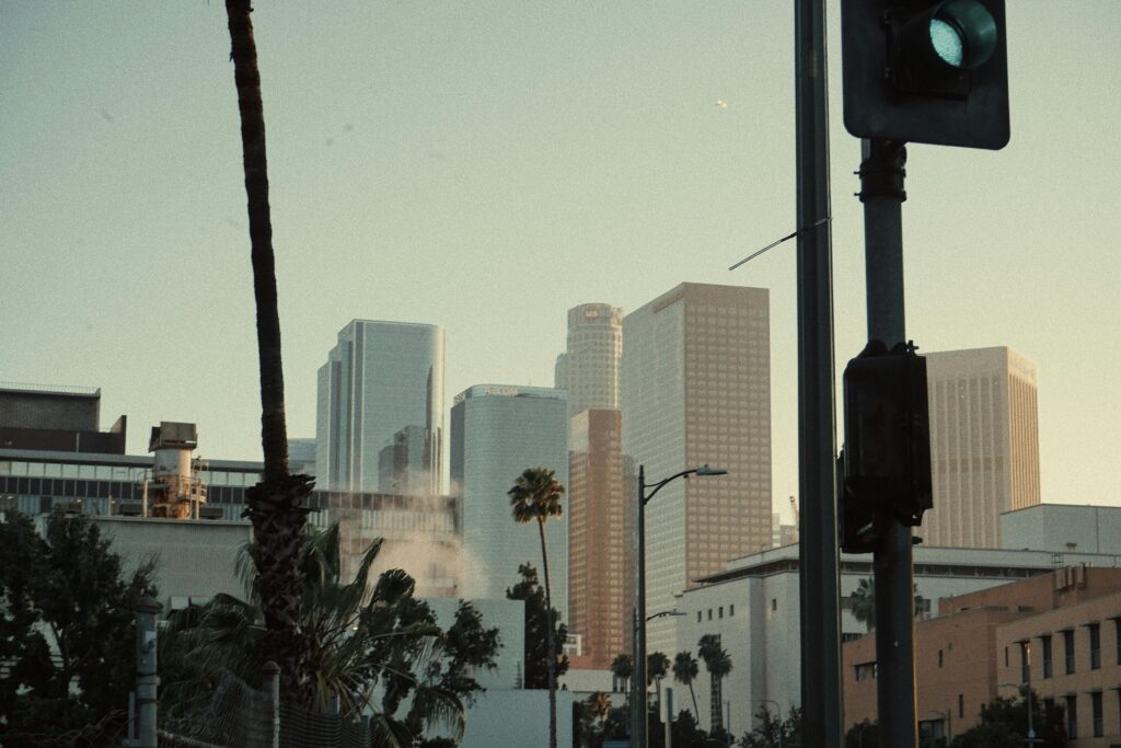 A striking view of tall skyscrapers in a city skyline with palm trees and traffic lights at twilight.